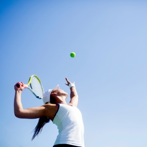 A woman is serving the ball. She is throwing the ball into the air with a tennis racquet in the other hand